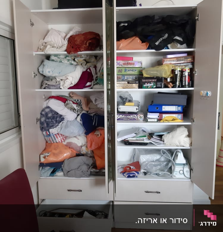 ארון פתוח עם בגדים, משחקים, קלסרים ומגהץ